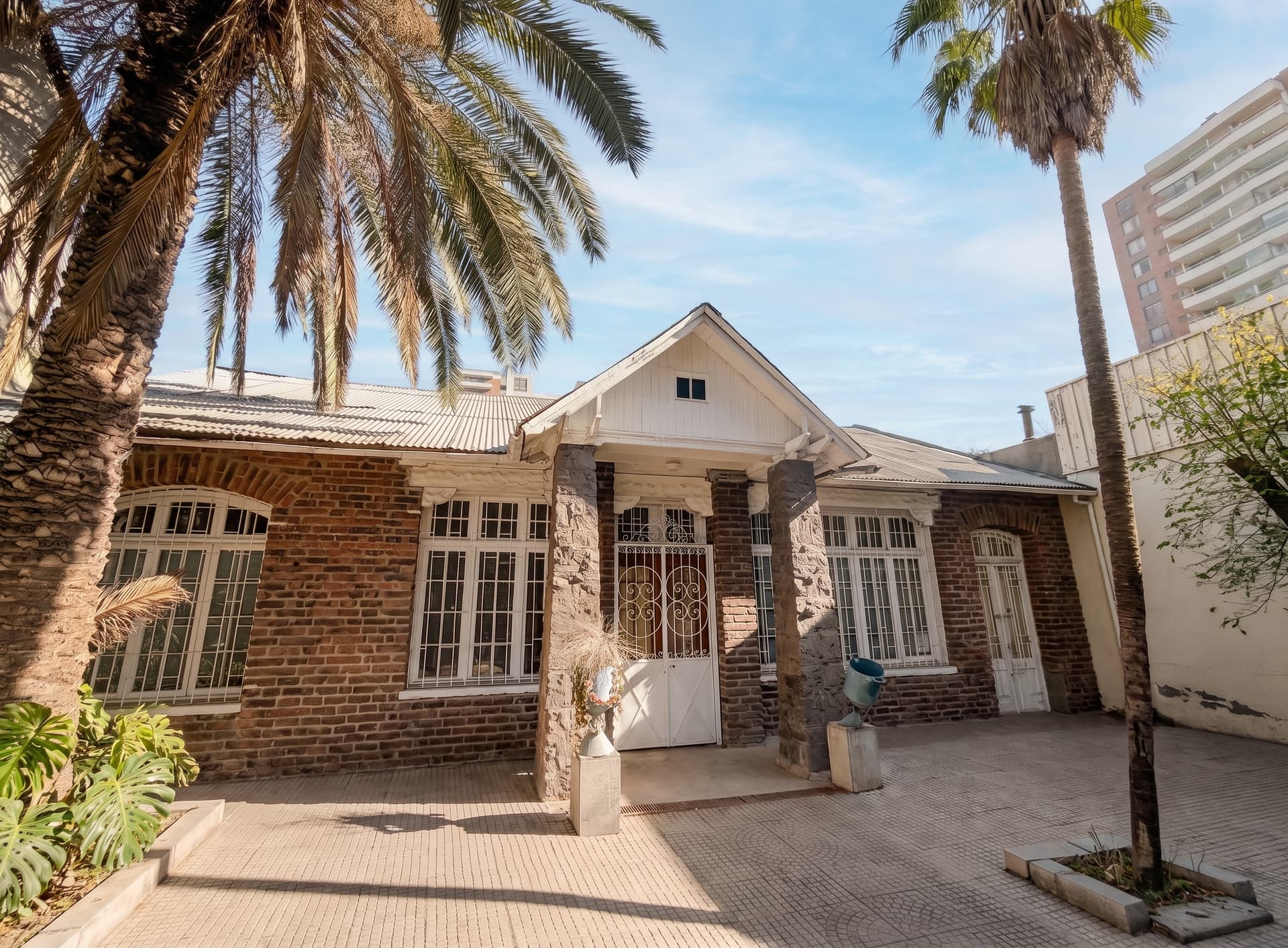 Fachada de la sede Salvador de Espacio Temporal en Ñuñoa: casa de ladrillo de arquitectura tradicional con pórtico blanco y palmeras